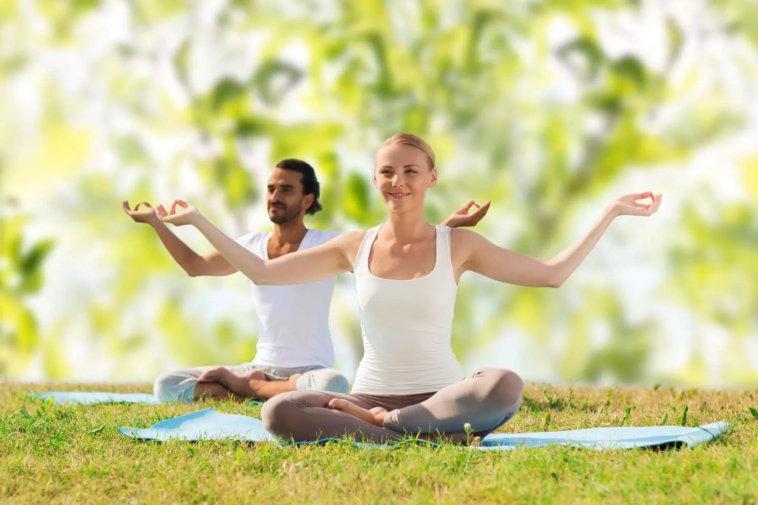 Two people sitting cross-legged on mats outdoors with their eyes closed